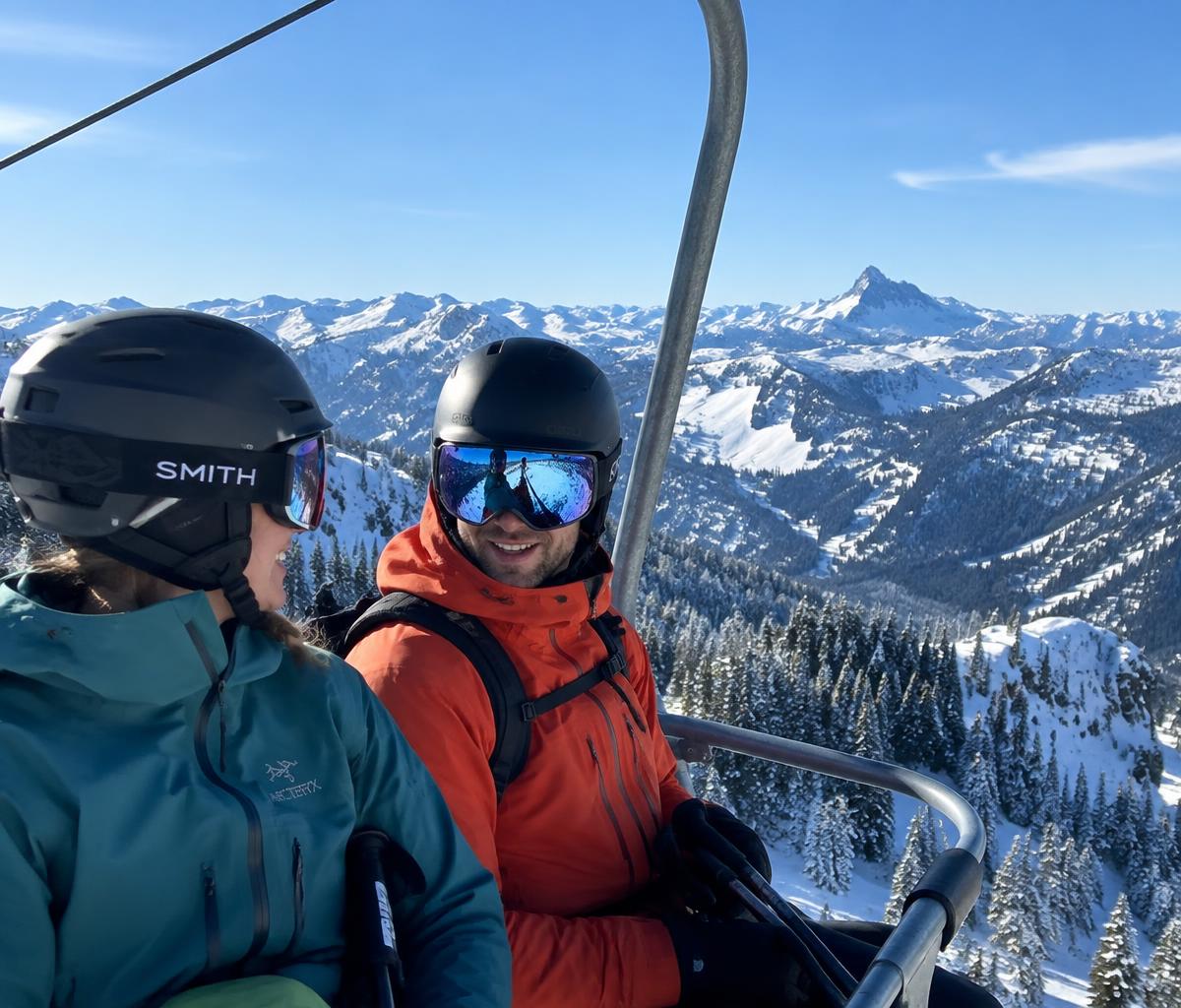Two skiers in helmets chatting and laughing on a chairlift