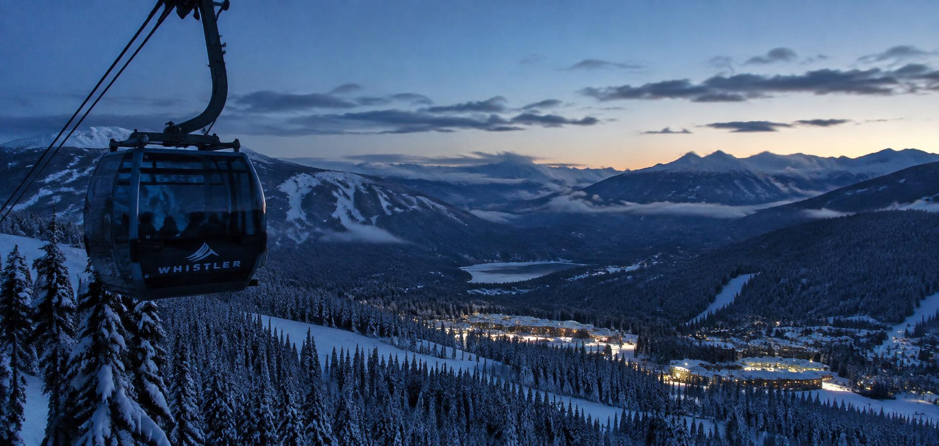 Glass gondola ascending Whistler mountain at dusk above the lit village